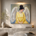 A square canvas painting of an angel with white wings and a yellow gown, displayed on a wall in a modern, sunlit living room with a marble console and round coffee table.