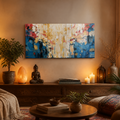 An abstract canvas painting with blue, white, red, and gold brushstrokes displayed on a warm beige wall in a cozy, styled living room setting with candles, plants, and a wooden console table.